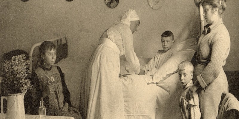 A black and white photograph of a nurse tending to a young boy in a hospital bed. There is another adult and two other young children in the room.