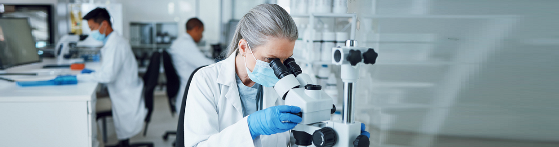 Research nurse working in a lab, looking into a medical telescope