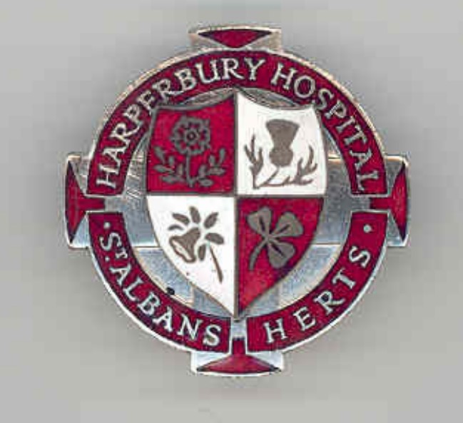 An enamelled badge in silver, red and white with shield in the centre which has been quartered displaying (from the top right): a thistle, a clover, a daffodil and a rose. These are surrounded by a red circular banner with the hospital name 'Harperbury-Hospital-St-Albans'